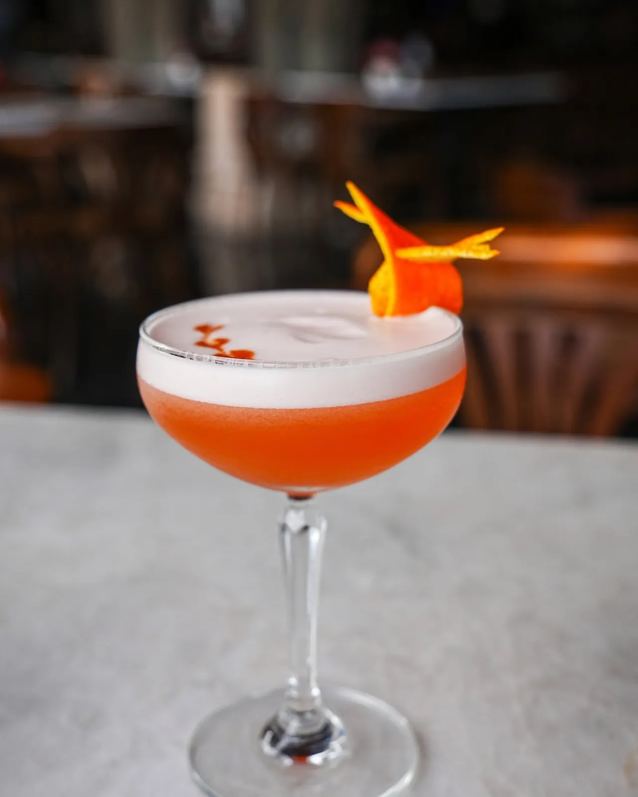 Orange cocktail with a foamy top and citrus garnish on the bar