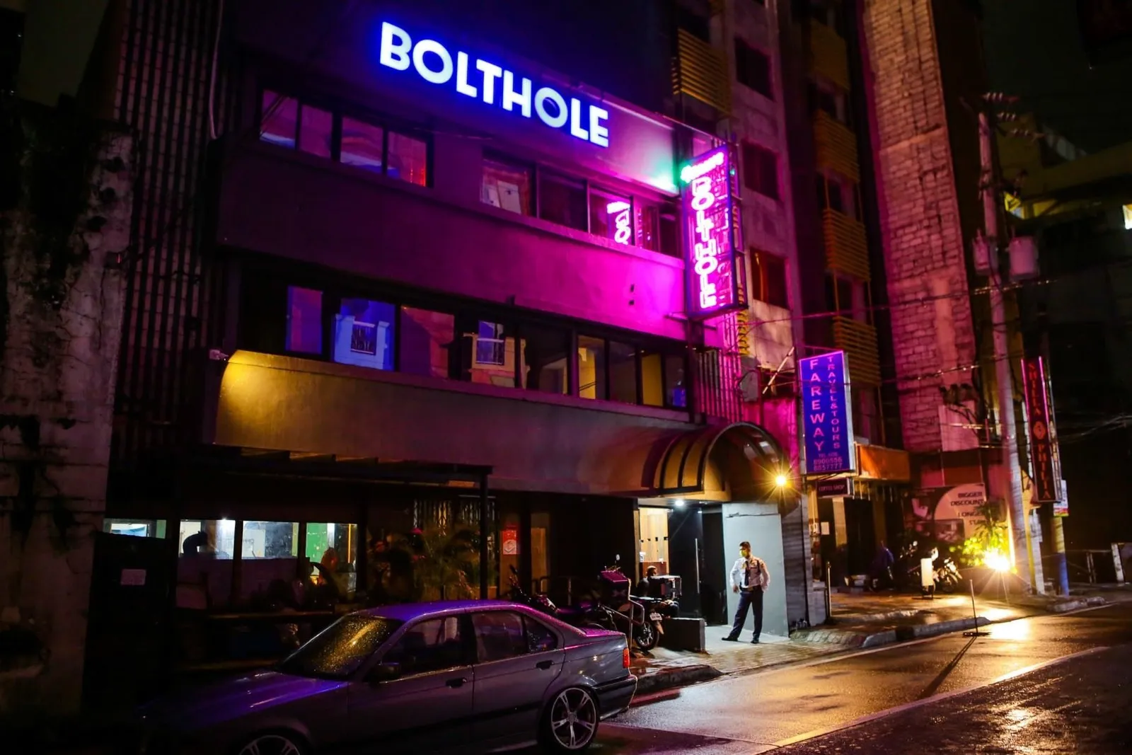 The Bolthole's entrance and balconies lit pink and blue at night.
