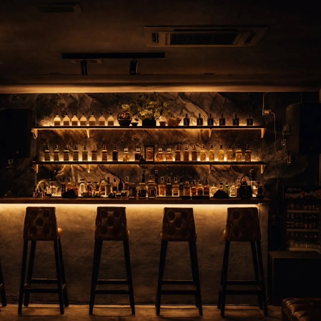 Low-lit bar with bottle shelves glowing behind the counter