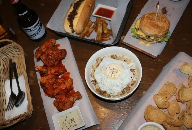 Table spread of a loaded hotdog, burger, wings, rice and chips