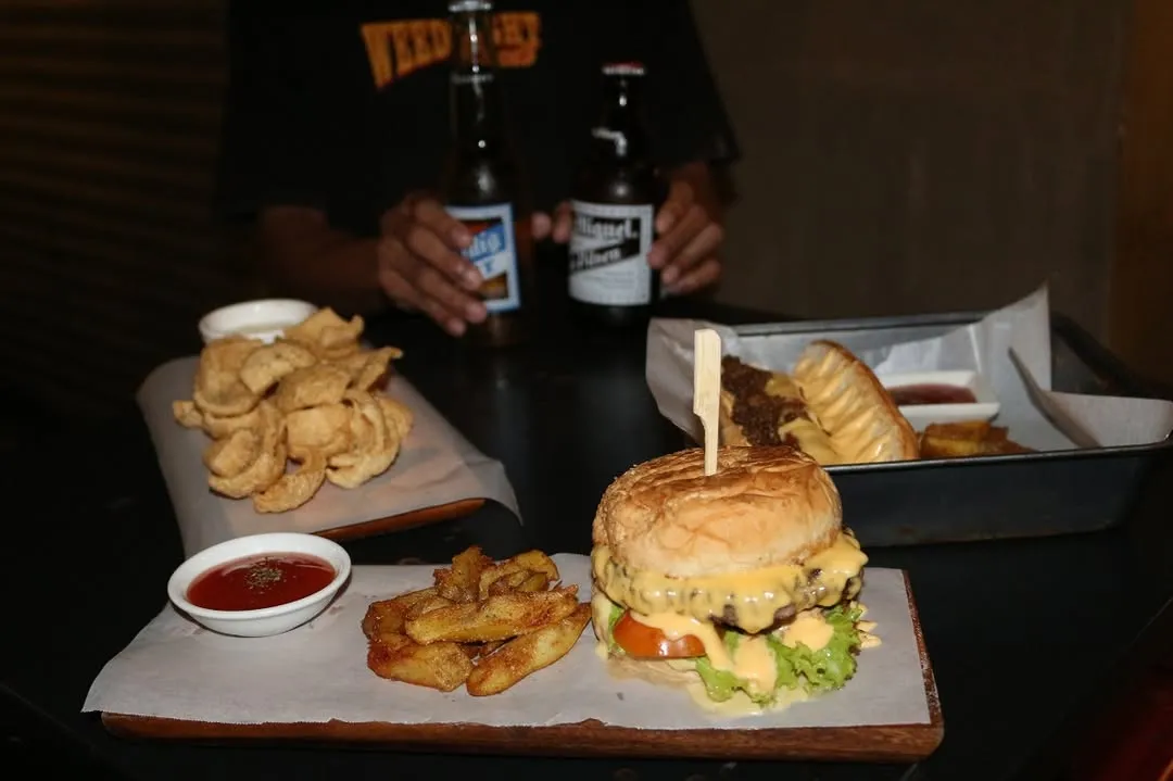 Cheeseburger and fries with hotdogs, chips and beer behind it