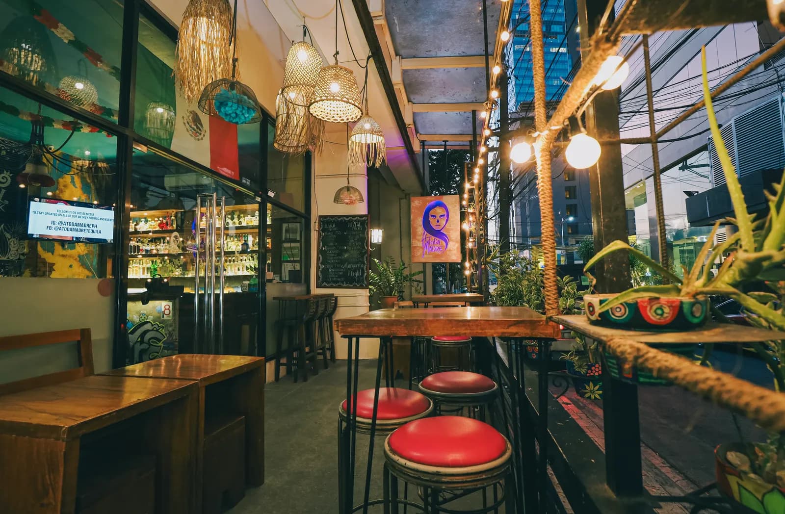Covered terrace with wooden tables, red stools and warm hanging lights