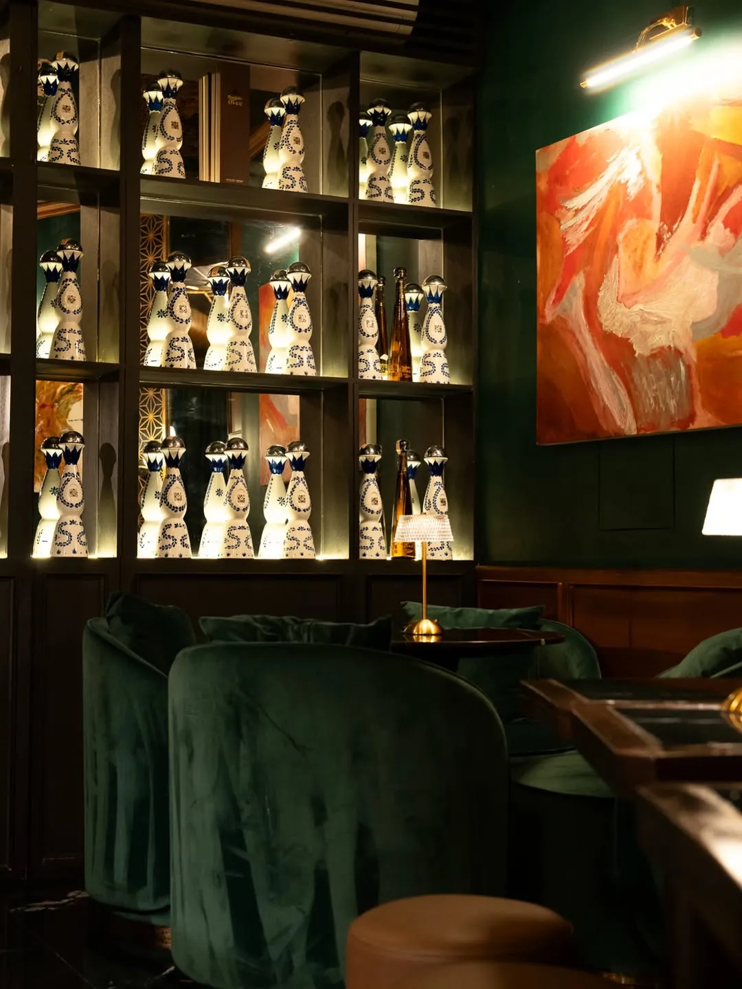 Dim green cocktail bar with bottle shelves and framed art