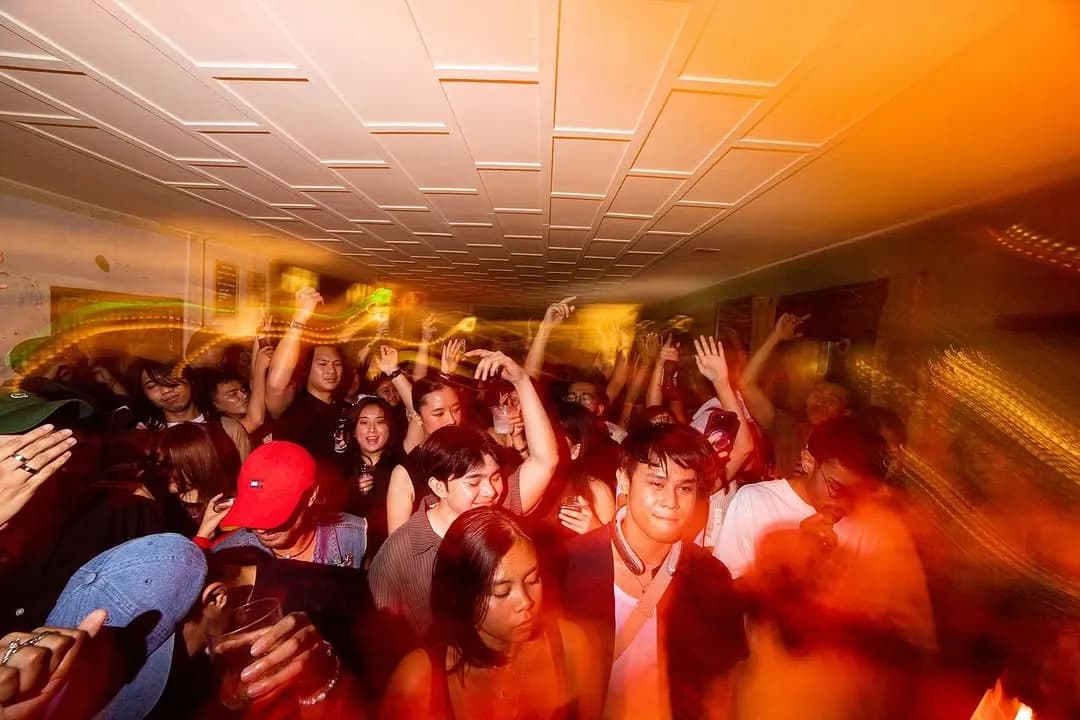 Packed dance floor with raised hands under warm orange lights at night