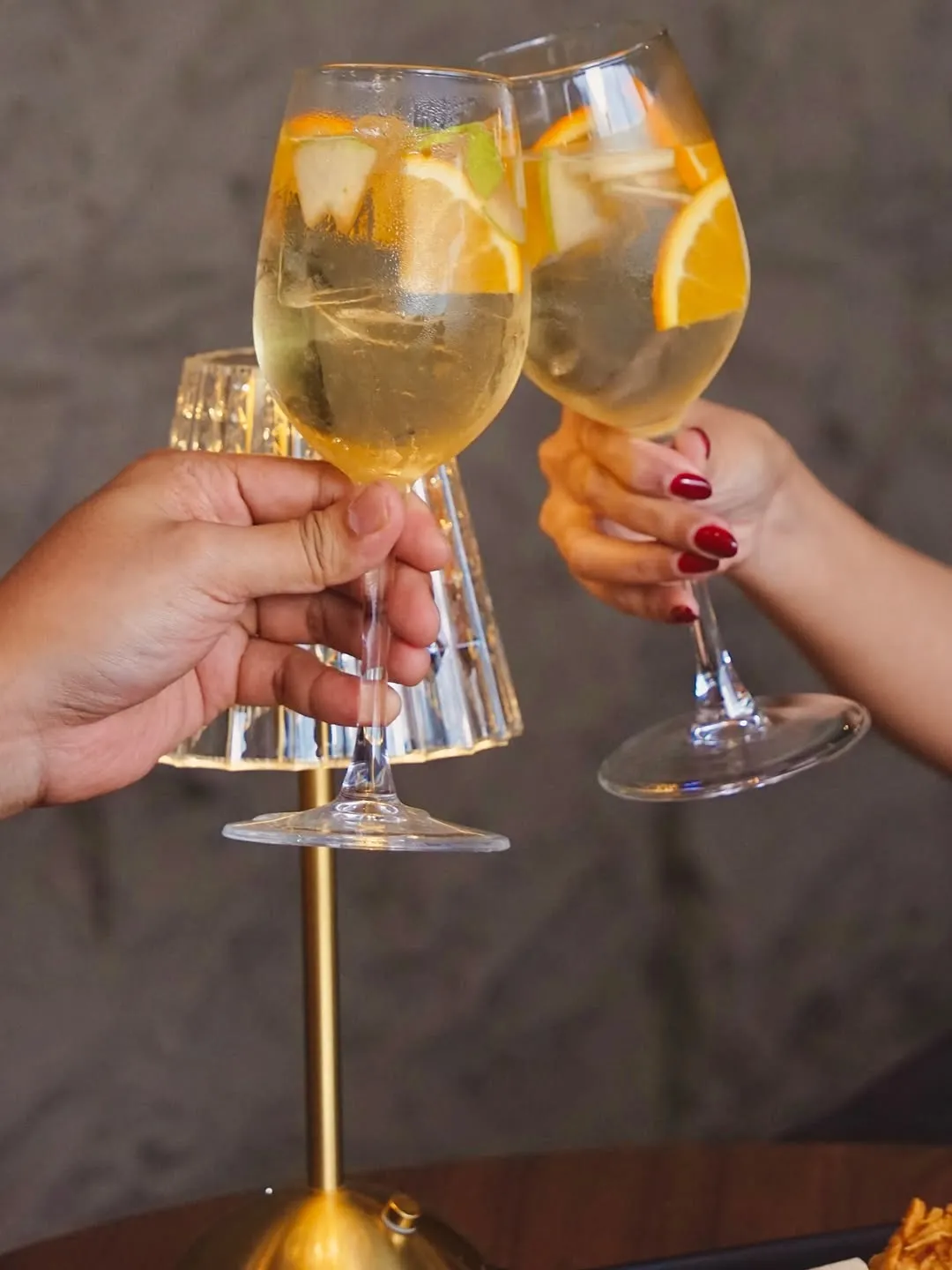 Two glasses of white sangria with citrus fruit raised for a toast.