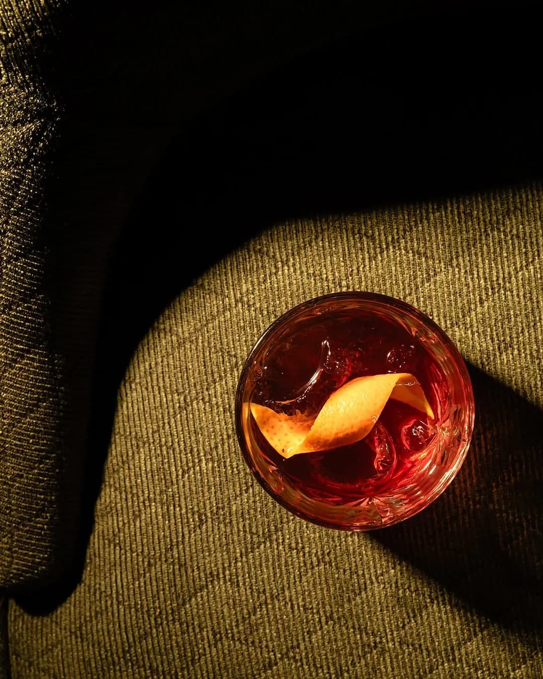 Red Mill cocktail with an orange peel on a green velvet chair