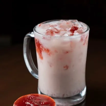 Pink iced milk drink in a clear glass mug.