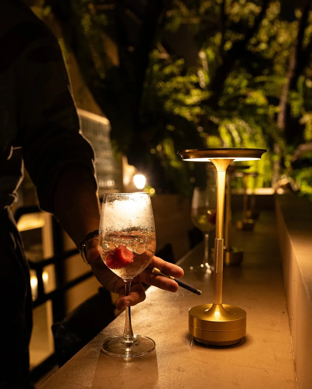 A fruit cocktail beside a brass table lamp on the bar at night.