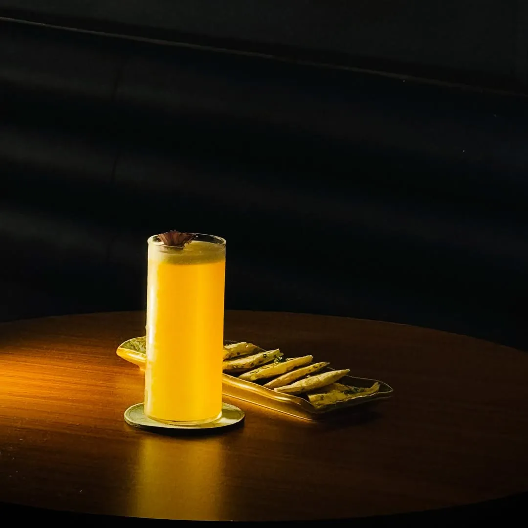 Tall yellow cocktail beside a plate of fries in the dark bar