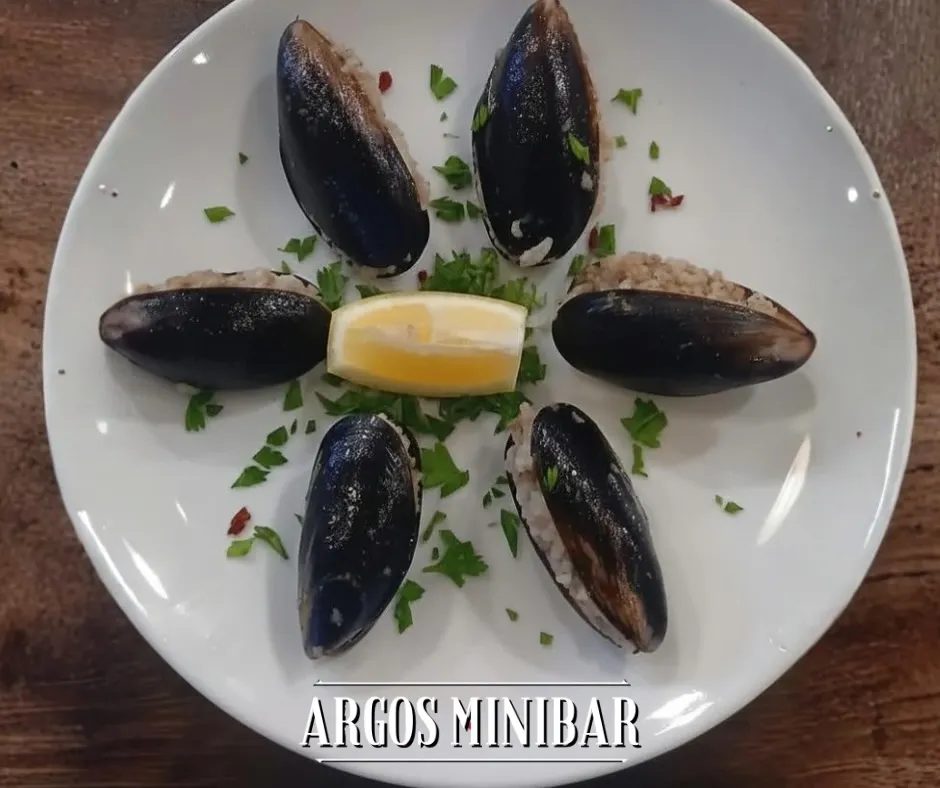 Midye dolma stuffed mussels arranged around lemon wedges on a white plate.