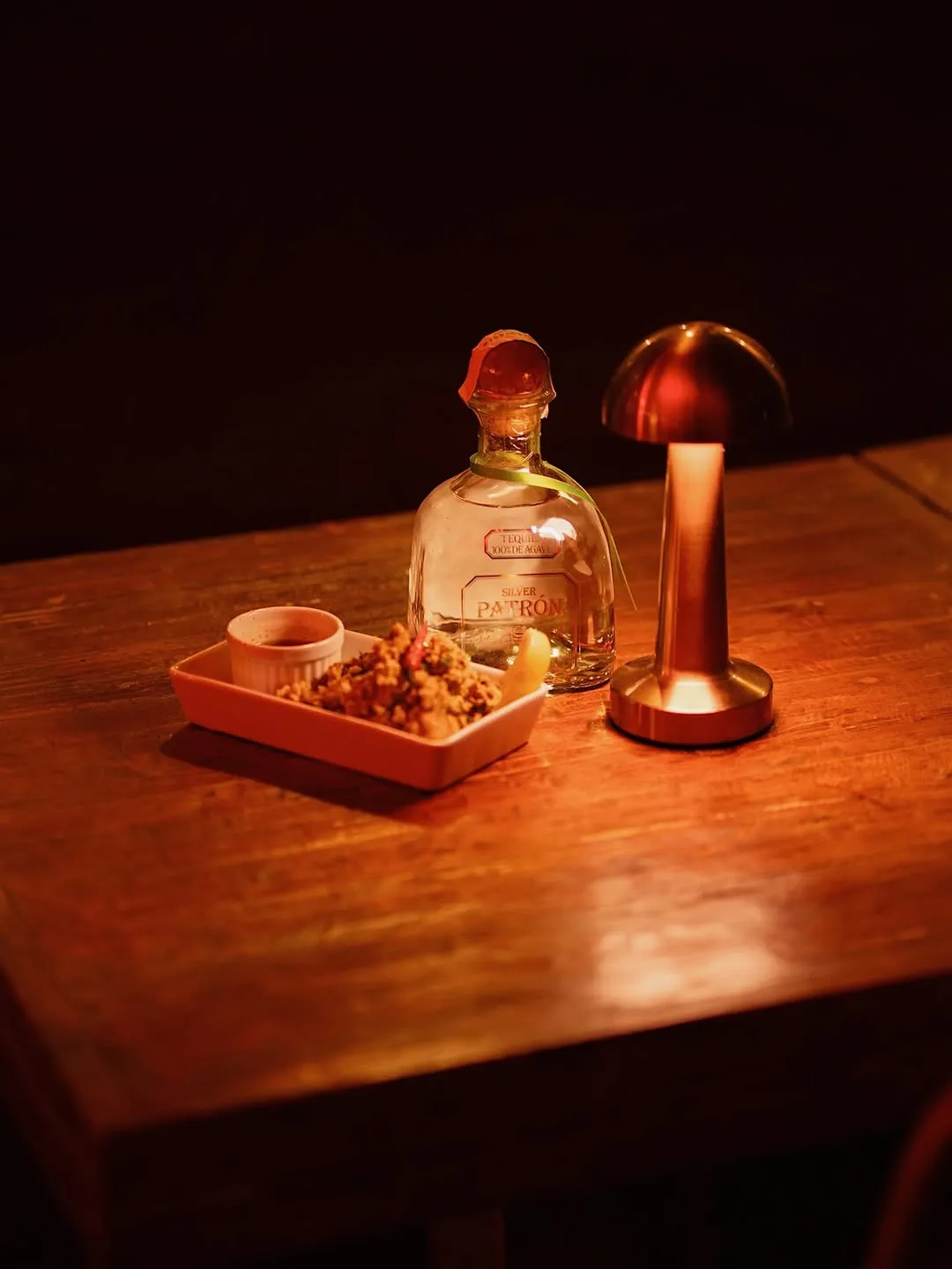 Bottle and bar chow on a lamp-lit table at night