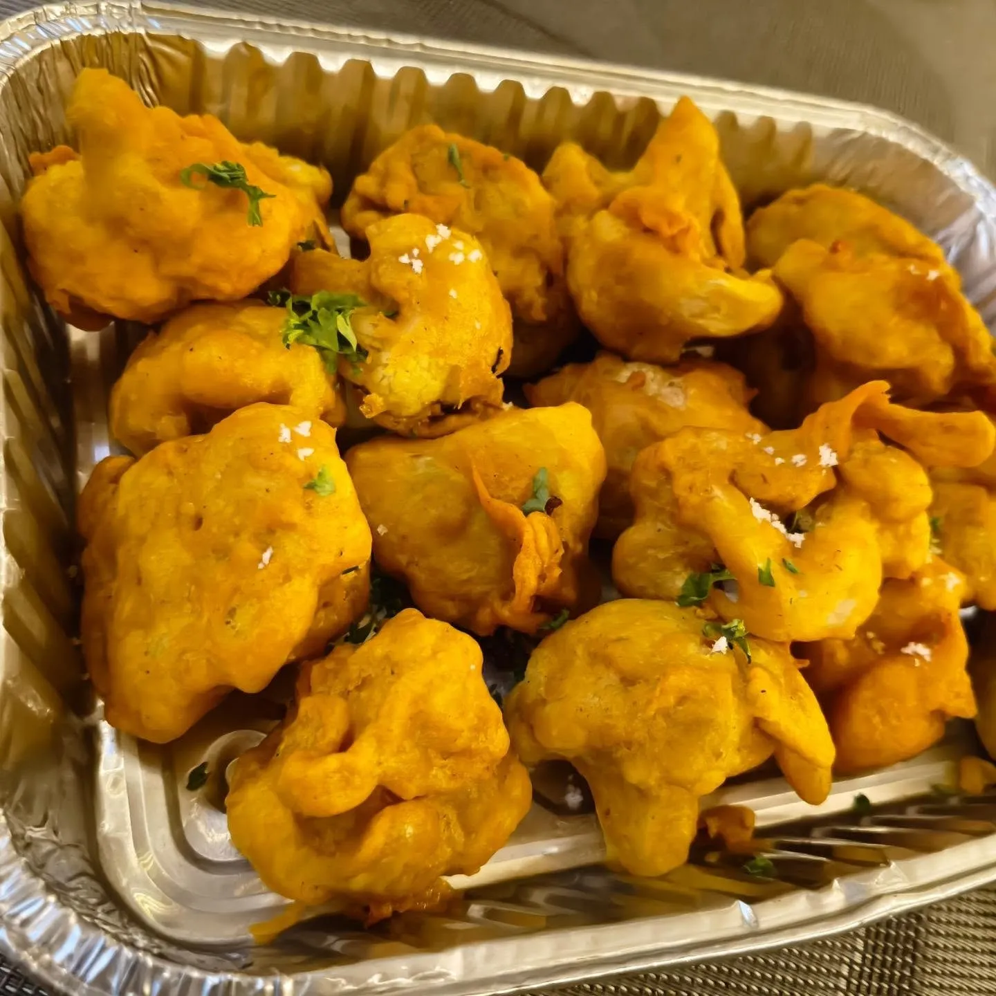 Tray of golden battered vegetable pieces garnished with herbs