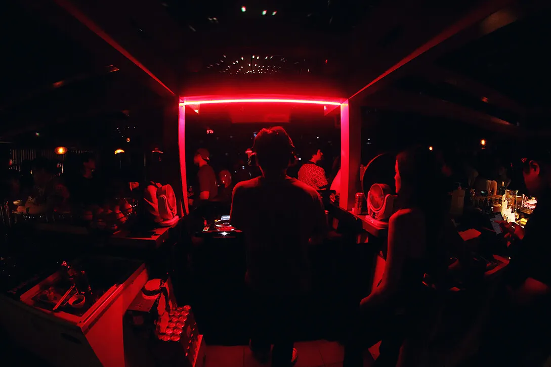 Crowded Kampai dance floor and DJ booth under red lighting at night