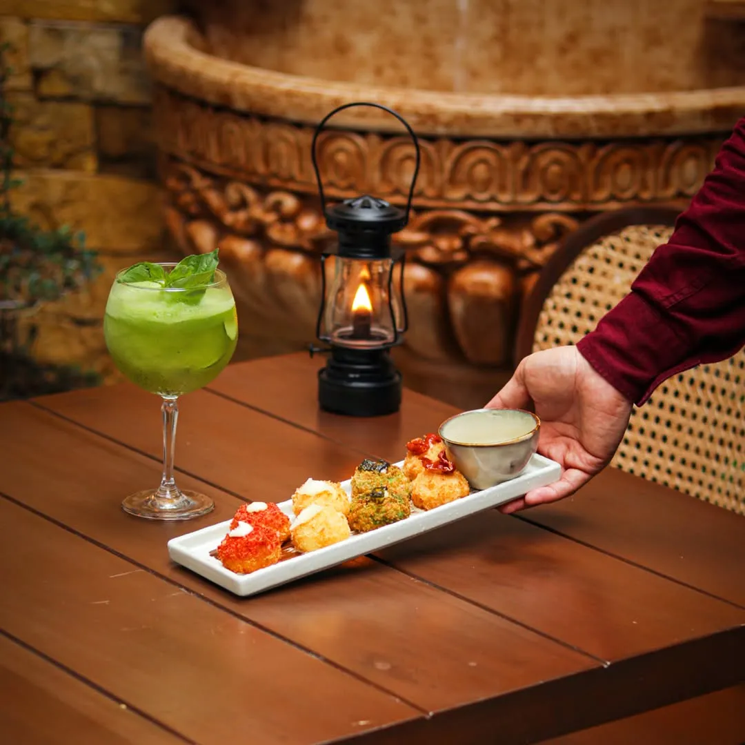 Green cocktail beside a plated bar snack on a wooden table