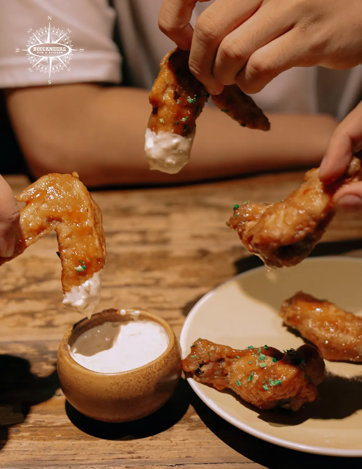 Glazed chicken wings being dipped into white sauce.