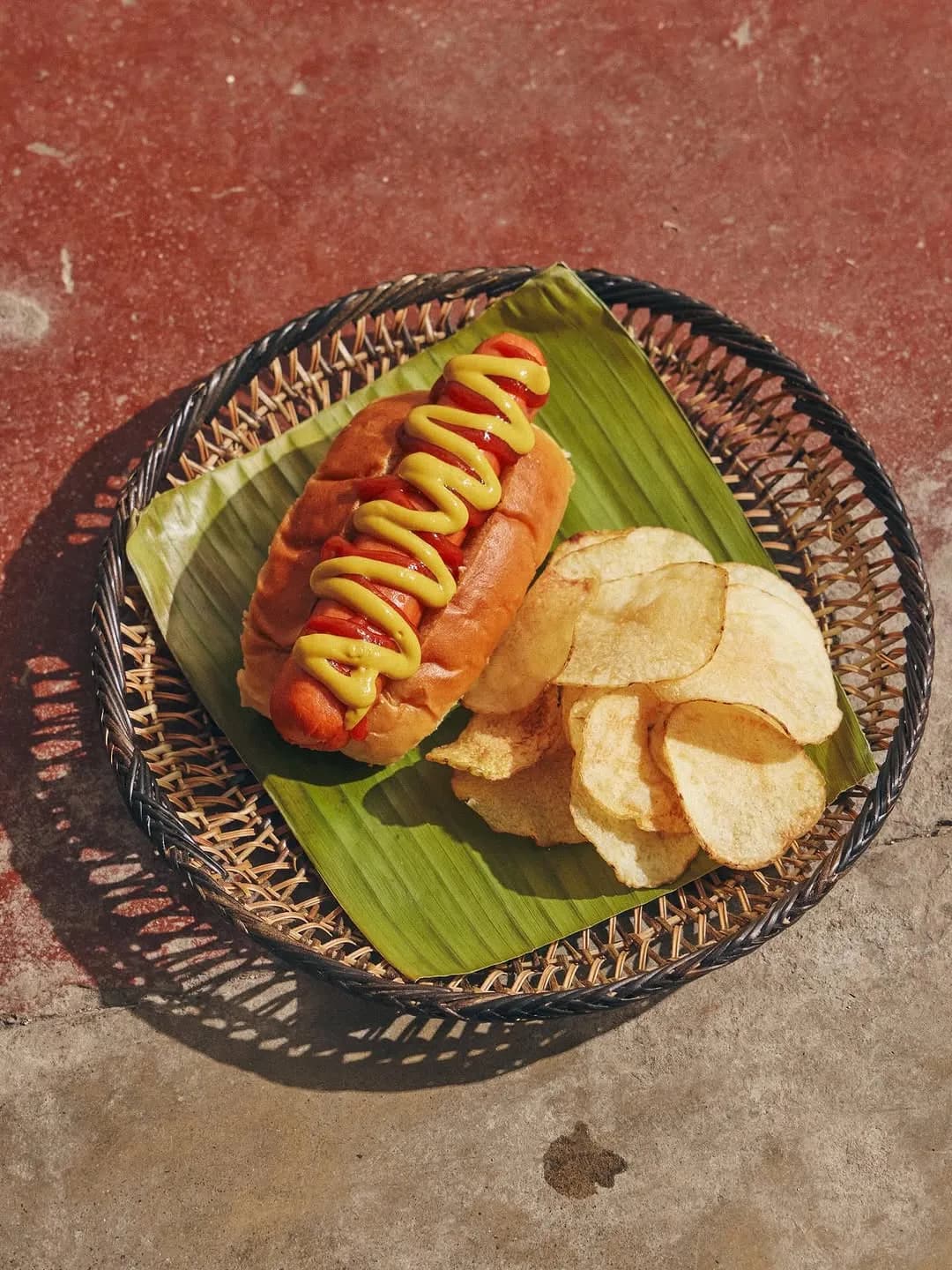 German frank in a potato bun with mustard and a side of potato chips
