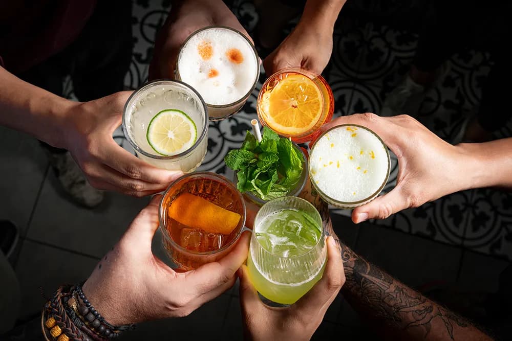 Six colorful cocktails held together in a toast