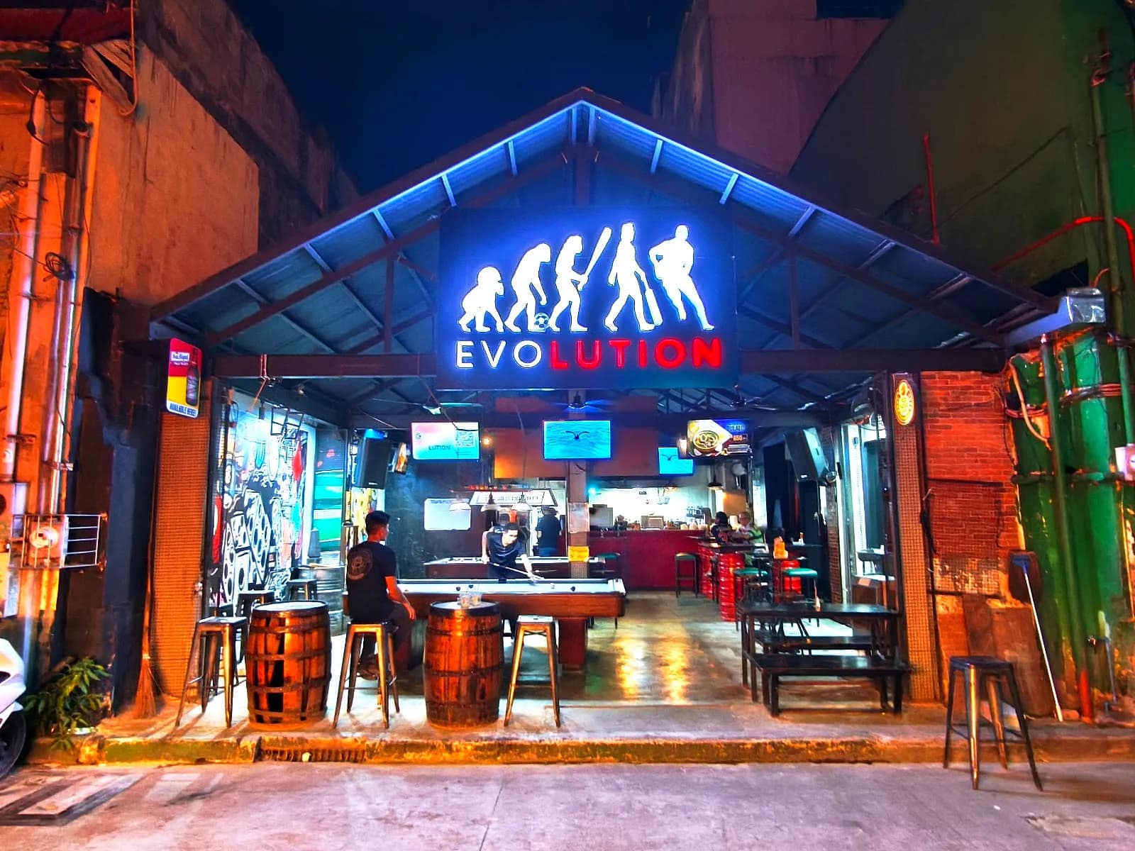 Open-front Evolution bar lit in blue at night with a pool table and screens inside