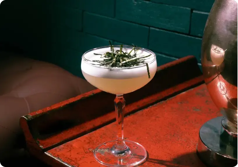 Pale cocktail in a coupe glass topped with strips of nori