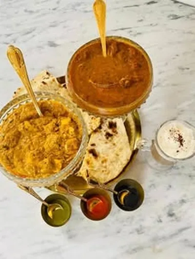 Two Indian curries with naan, rice and condiments on a marble table