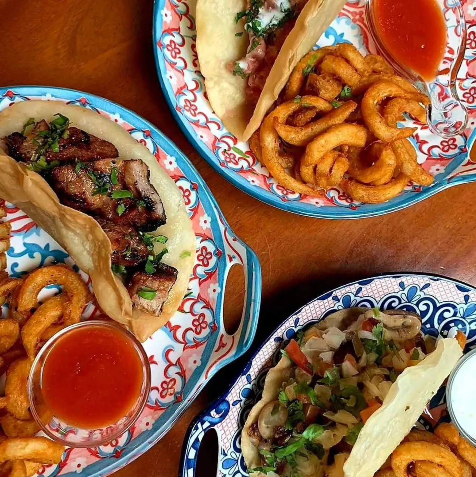 Three plates of tacos with curly fries and dipping sauces.