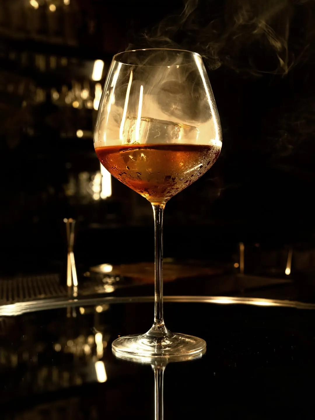 An amber cocktail in a stemmed glass on the bar.