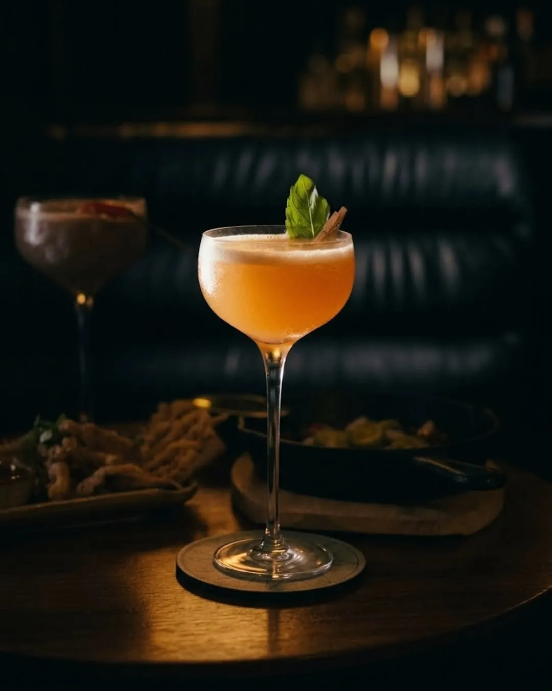 Orange cocktail in a coupe on a dim bar table