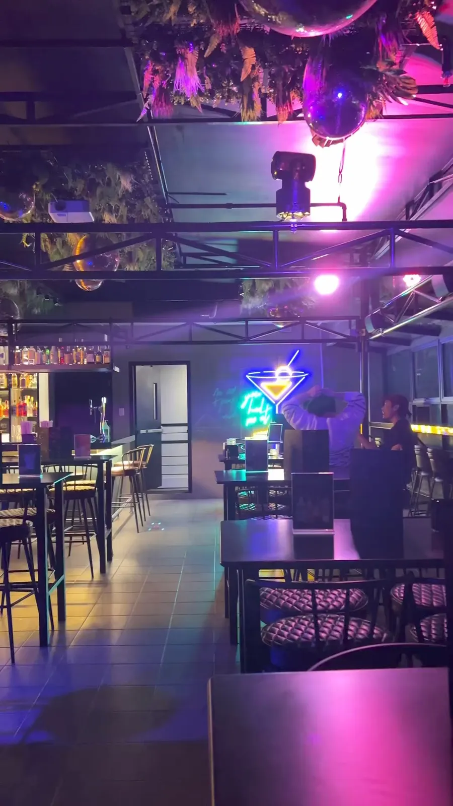 Mad Sky's rooftop dining room lit in pink and blue, with bar shelves and high tables.