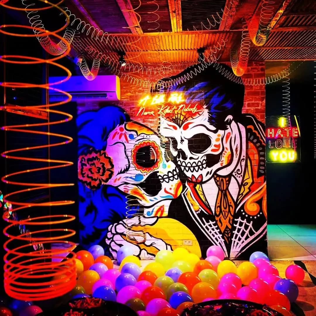 Neon-lit interior with a skeleton mural, hanging decorations and ball pit.