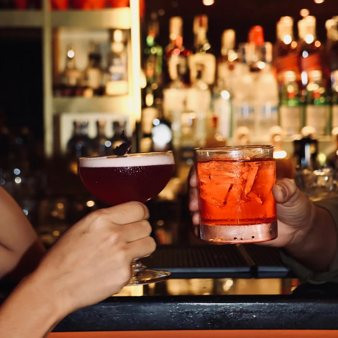 Red cocktail held in front of the bar shelves