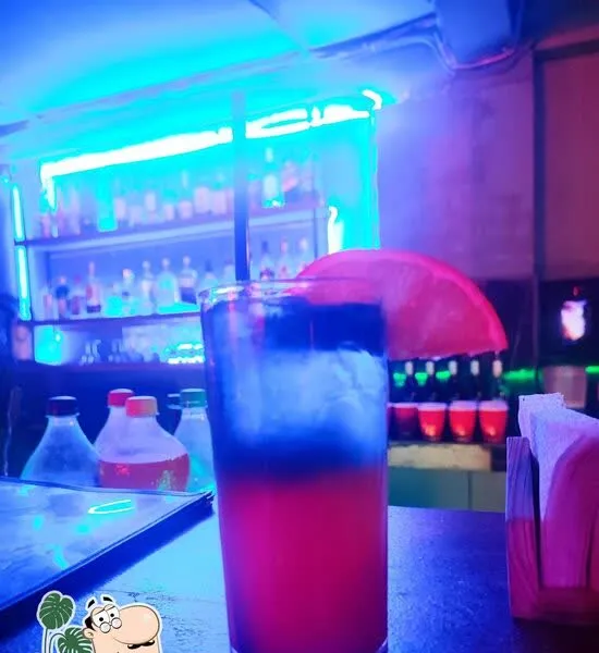 A tall red-and-blue cocktail on the bar under neon lighting.
