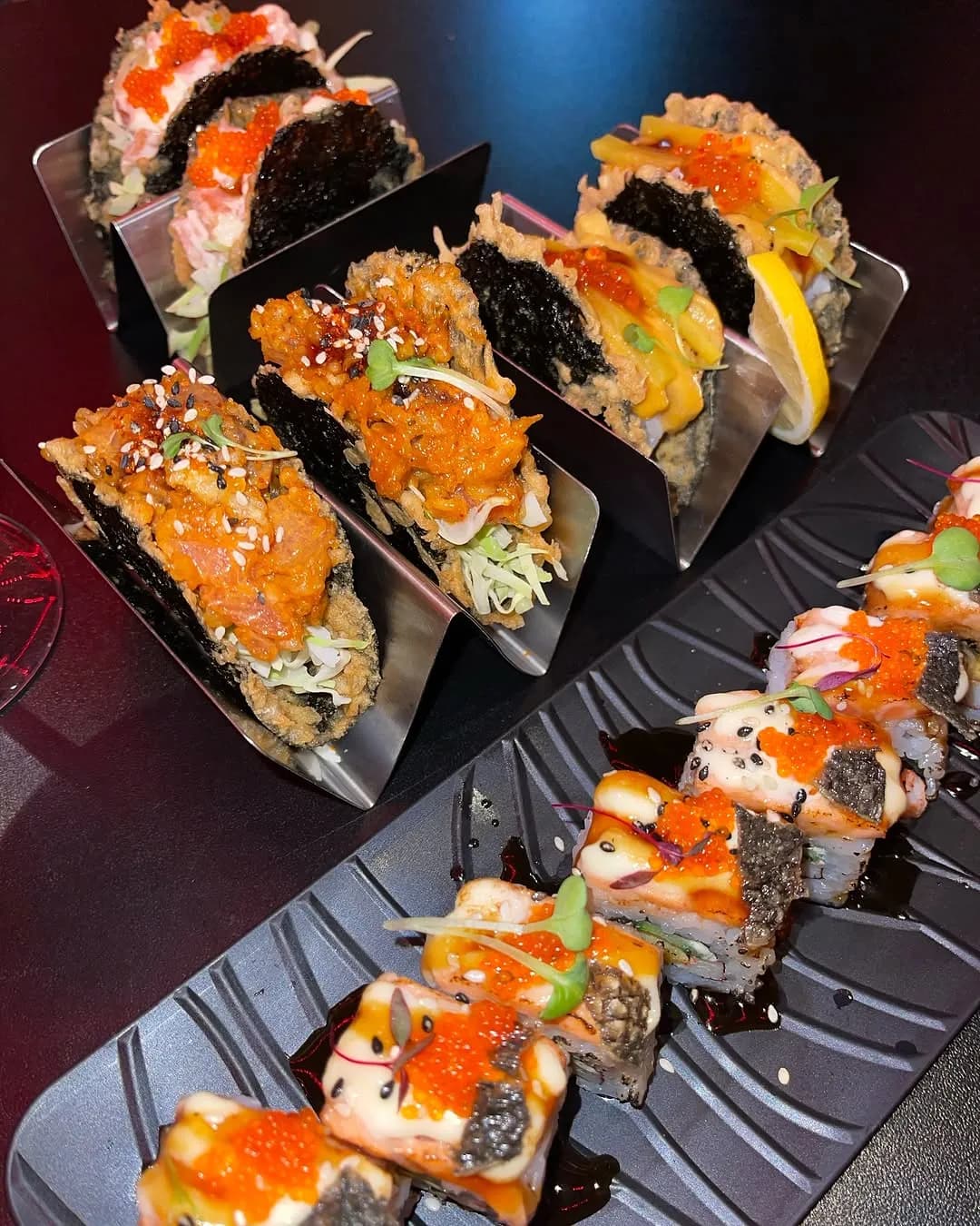 Rows of sushi rolls topped with salmon and sauces.
