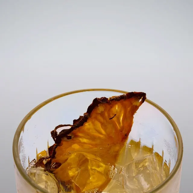 A clear cocktail over ice finished with a dehydrated pineapple slice.