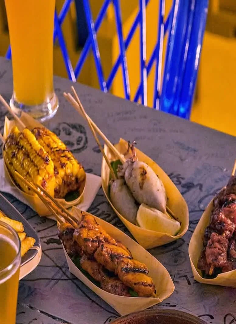 A table spread of grilled corn, skewers and other bar snacks with craft beer.