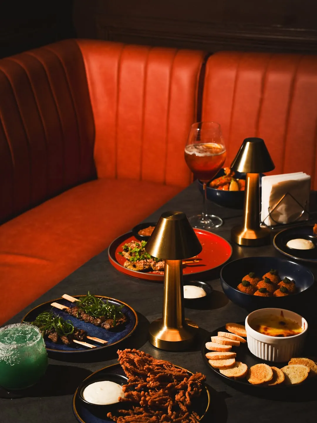 Red leather booth set with small lamps, cocktails and bar food