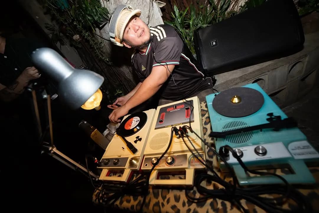 DJ playing vinyl beside vintage turntables and tape decks at night