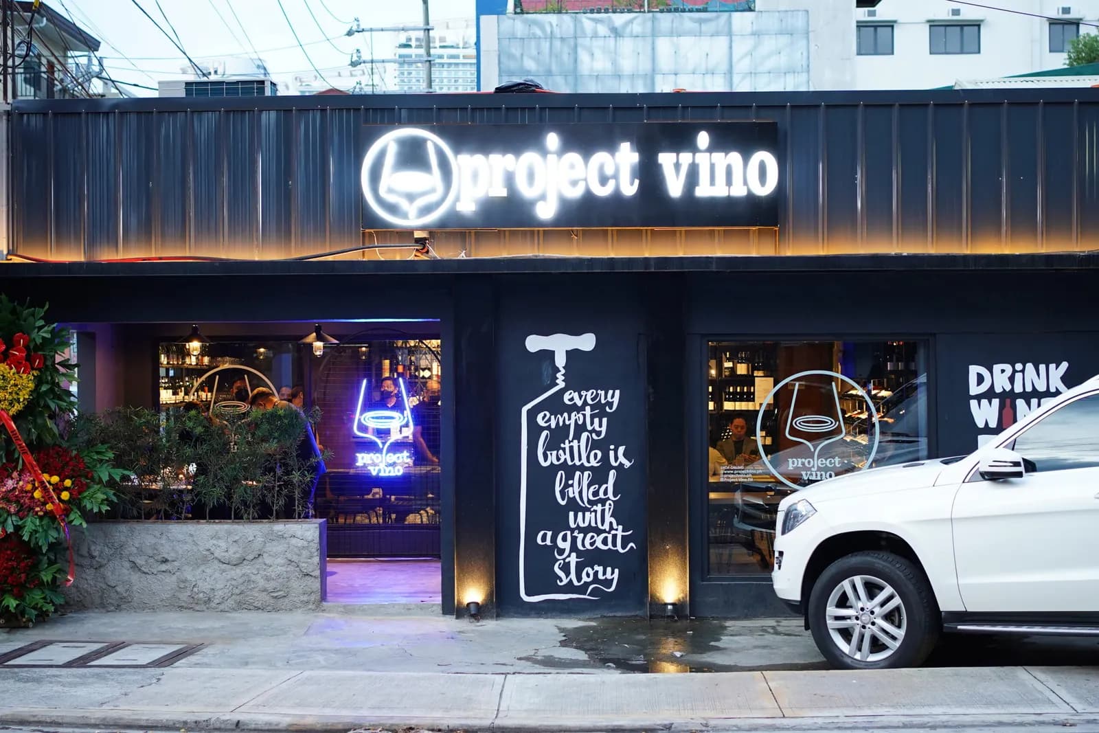 Project Vino's black storefront and illuminated sign at dusk.