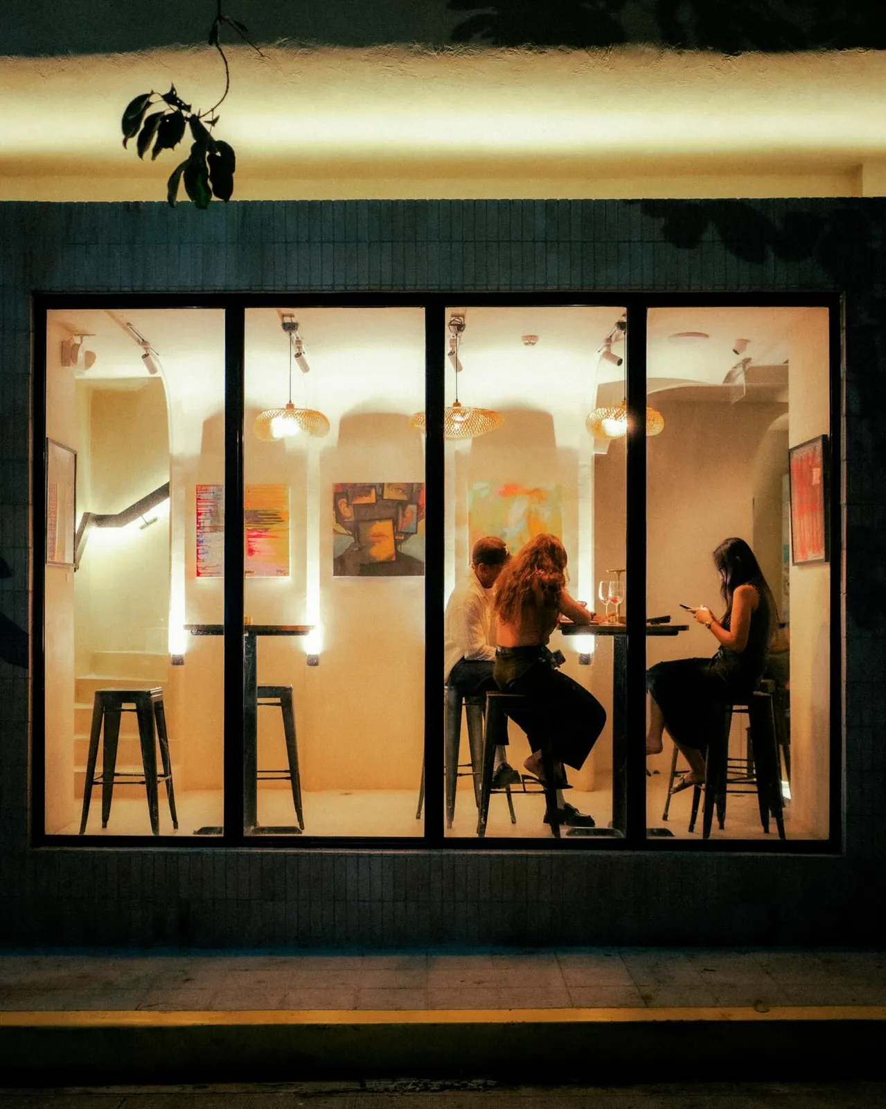 The café's lit windows at night, with guests at high tables inside.
