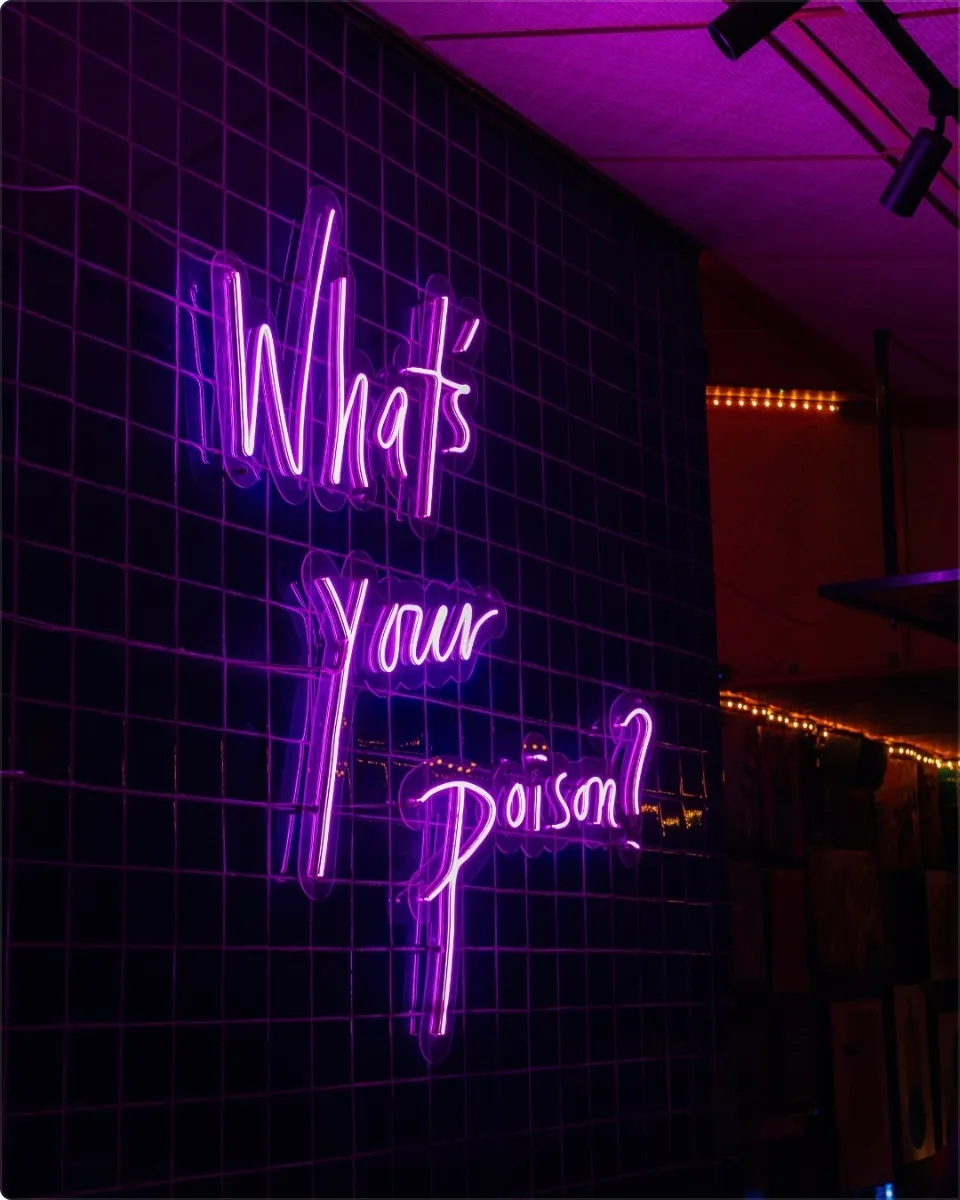 Purple What's Your Poison neon sign inside the dim bar