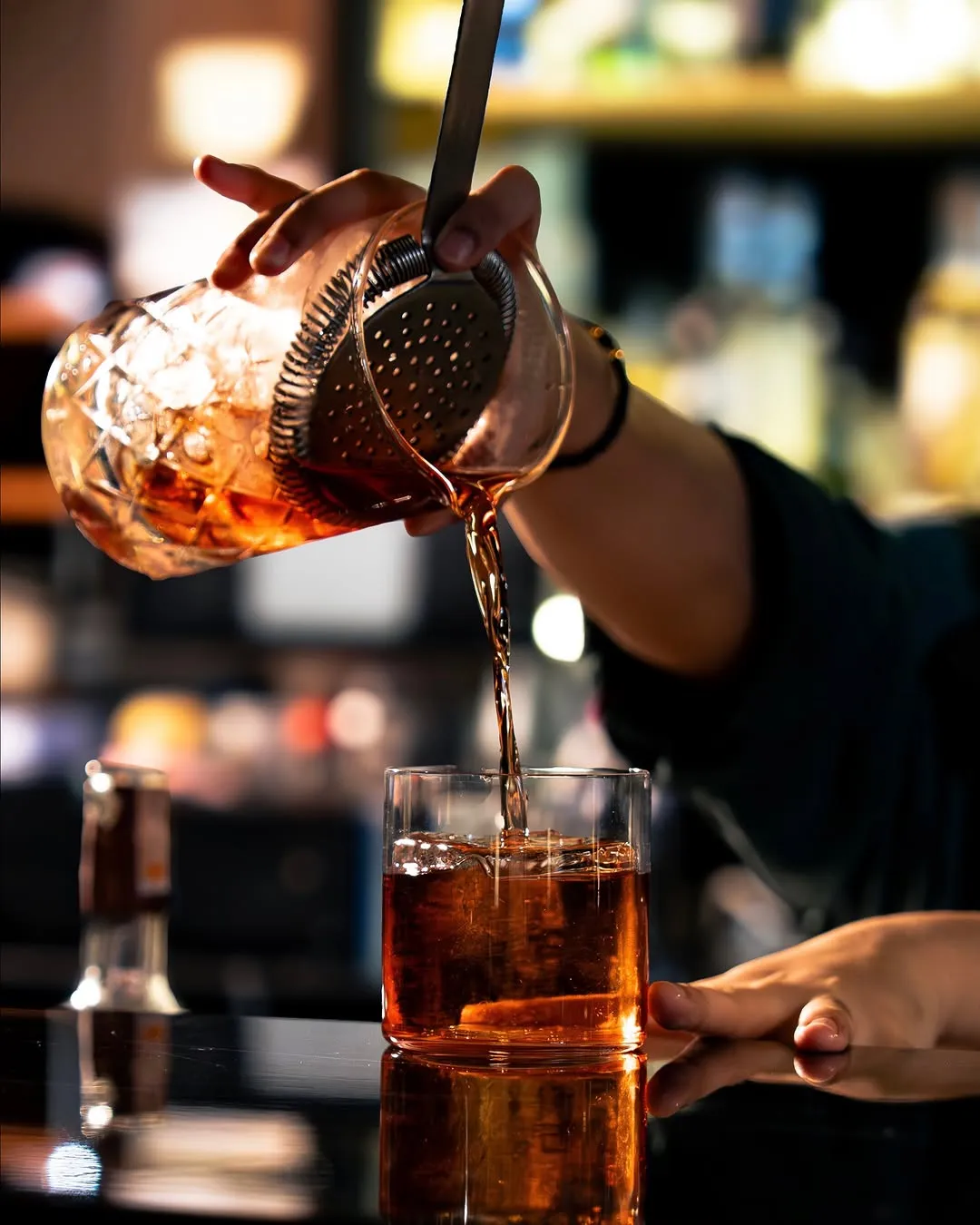 Bartender pouring an amber cocktail into a rocks glass