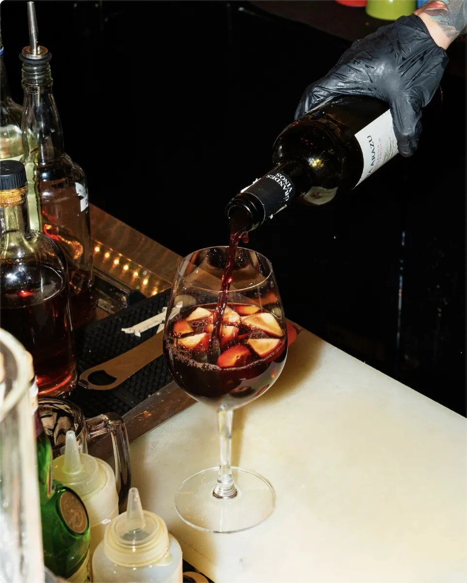 Red wine cocktail being poured over fruit at the bar