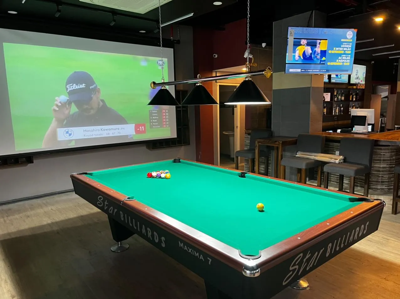 Pool table facing a large sports screen inside the bar