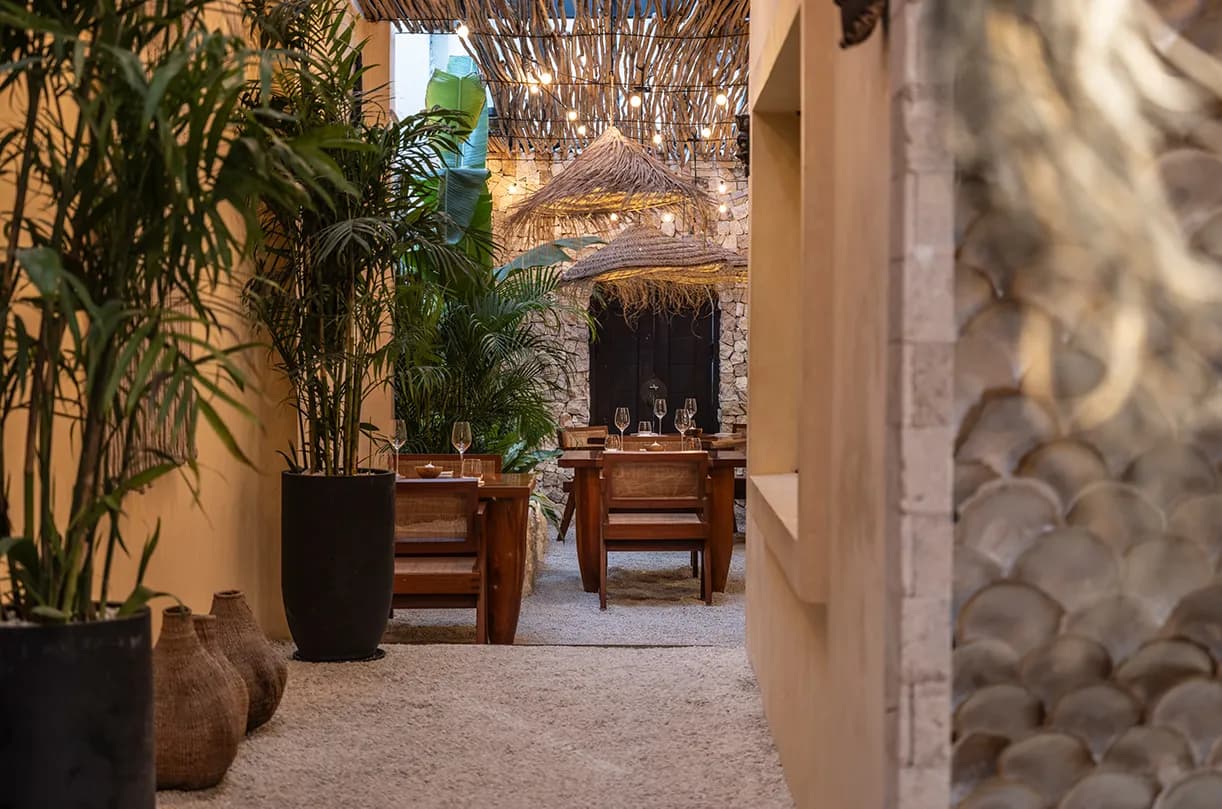Plant-filled courtyard dining area with wooden tables and warm overhead lights.