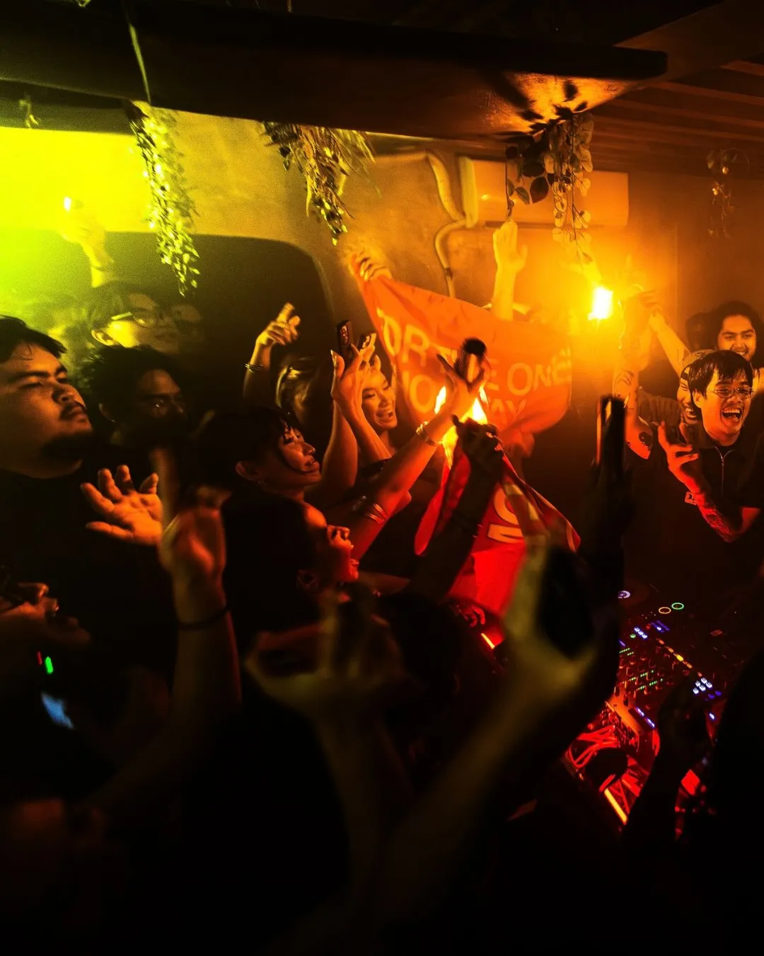 A packed dance floor under orange and red club lighting.