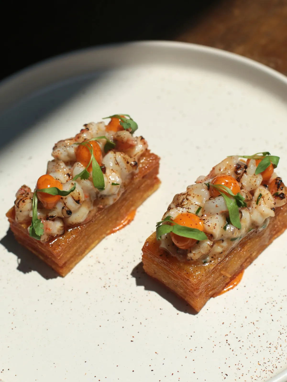 Two crisp potato pavé pieces topped with grilled shrimp and herbs