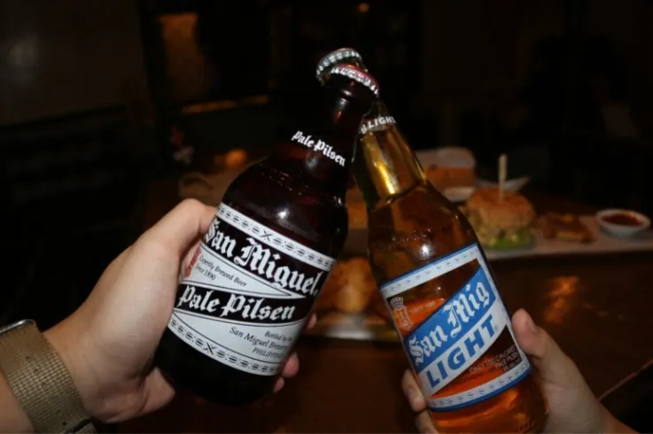 Two bottles of San Miguel beer raised over a dark table
