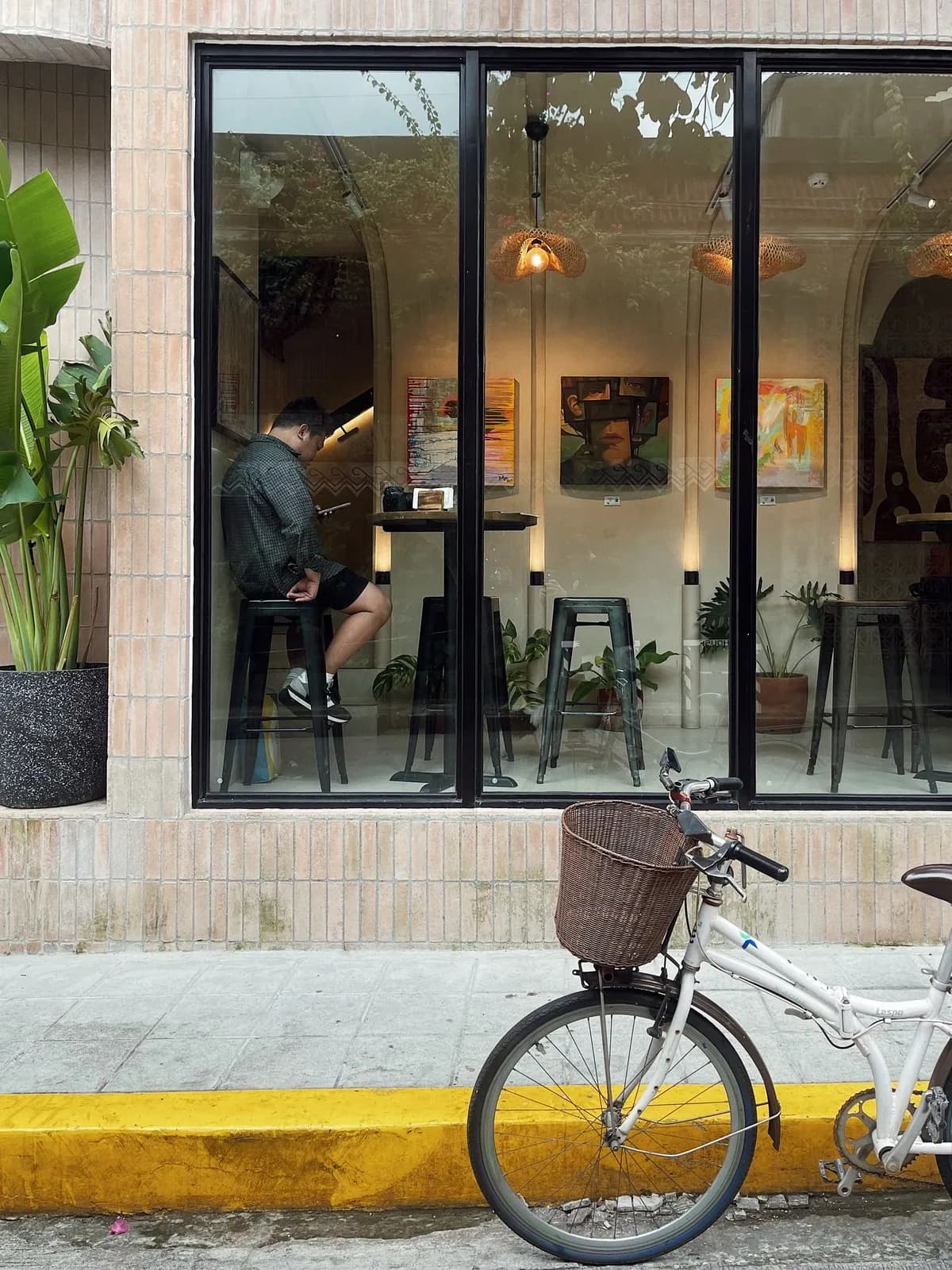A bicycle parked by the café's big window, with art on the walls inside.