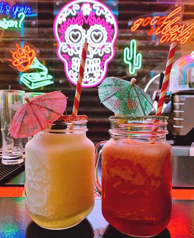 Two frozen cocktails in handled jars on the neon-lit bar.