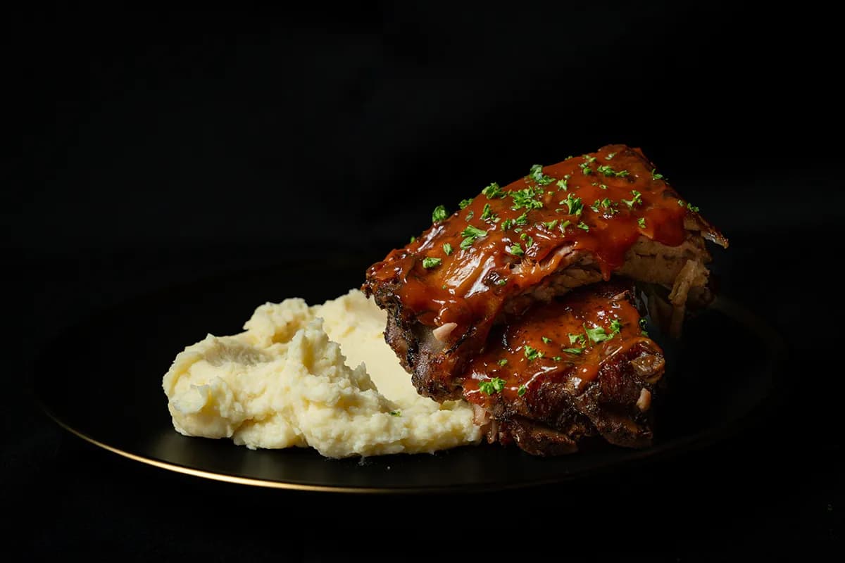 Barbecue ribs with mashed potatoes on a black plate