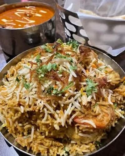Prawn biryani in a metal serving bowl with curry behind it